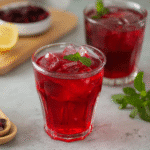Hibiscus Tea Drink Recipes : Refreshing & Healthy Guide 5 Hibiscus Tea Drink Recipes – A glass teapot and cup filled with deep red hibiscus tea, surrounded by dried hibiscus petals and fresh mint leaves.